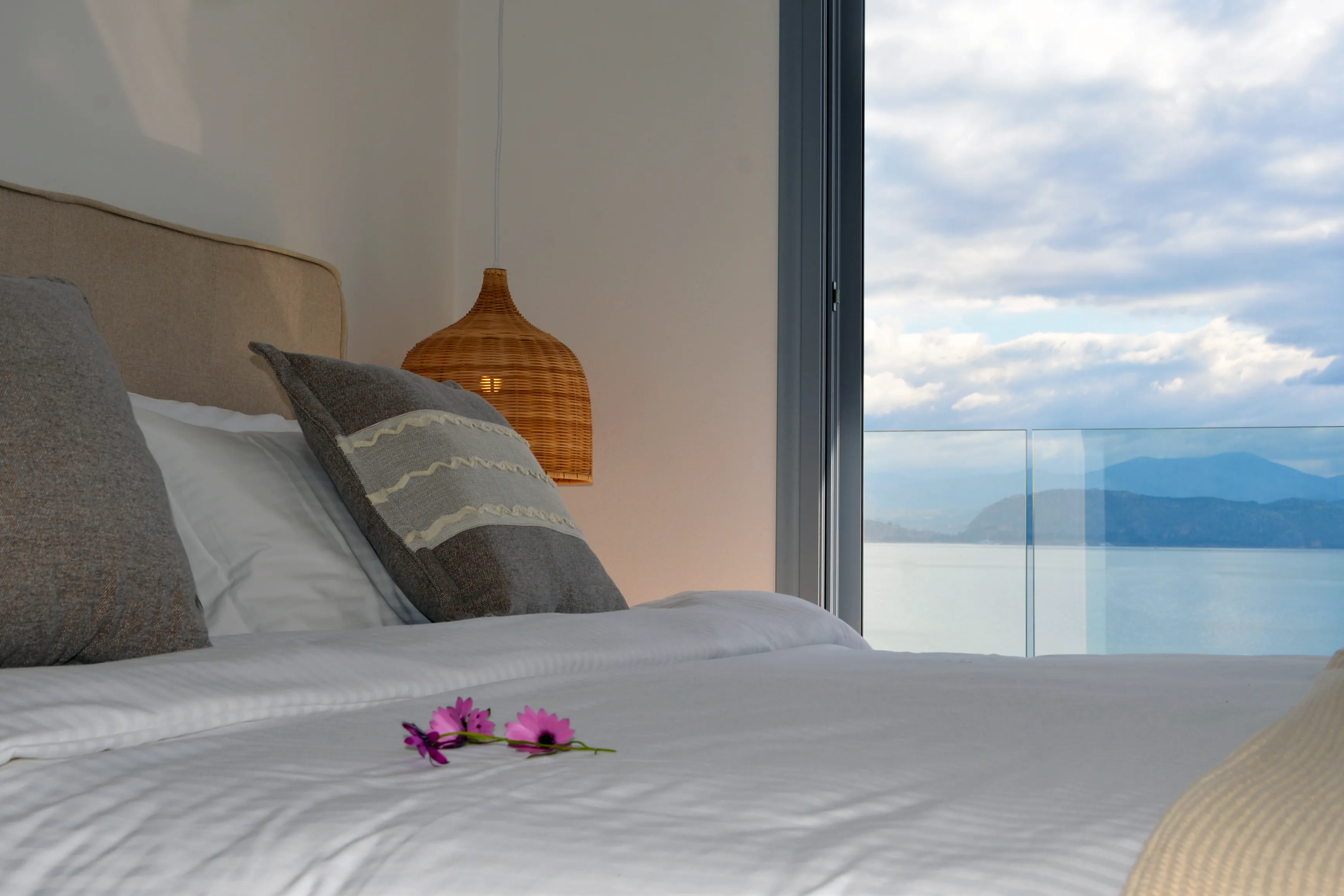 Euros bed under a wicker pendant with the gulf beyond the balcony rail