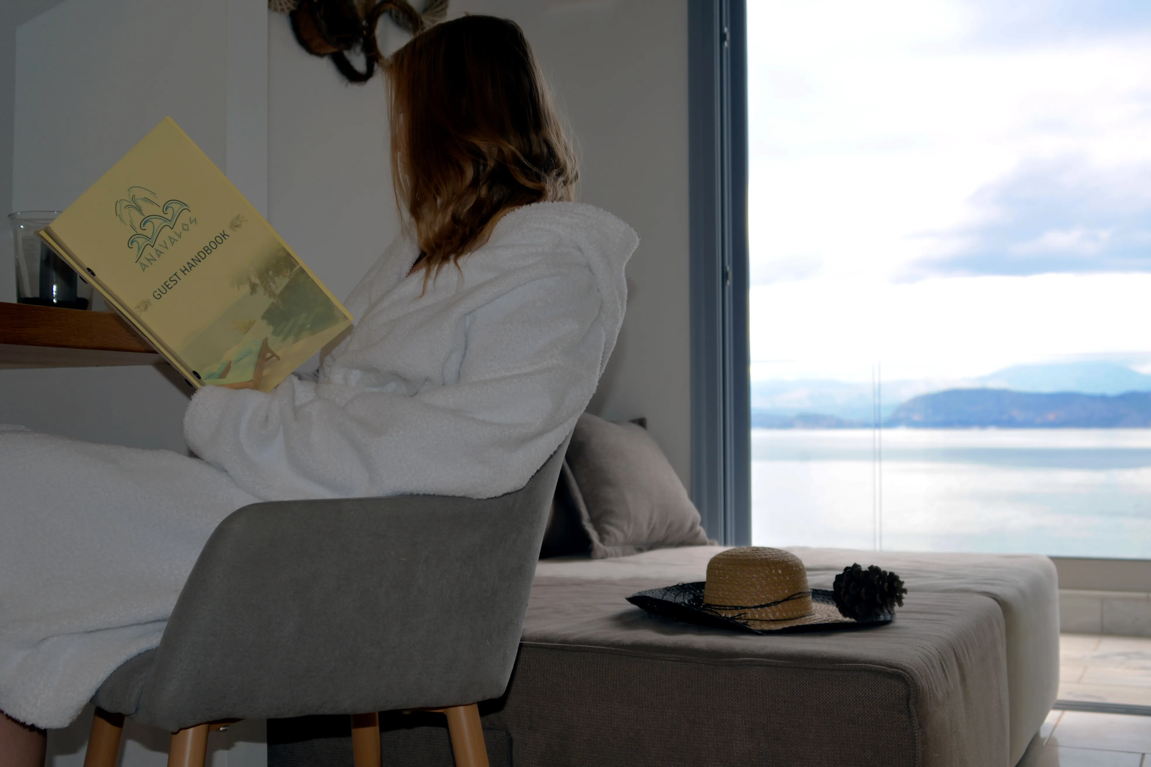 Guest reading in the Notos armchair beside the broad sea-view window